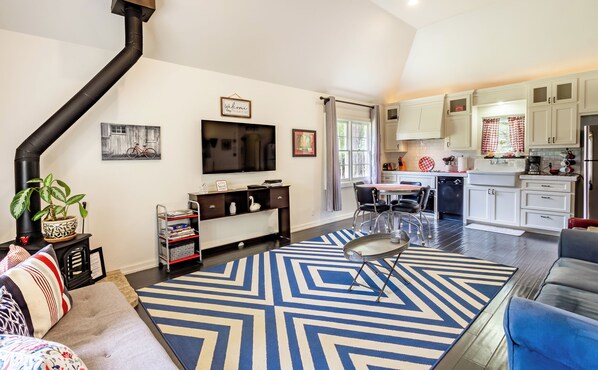 A living room with a sofa, a coffee table, and a TV. There is a kitchen with cabinets and a dishwasher.