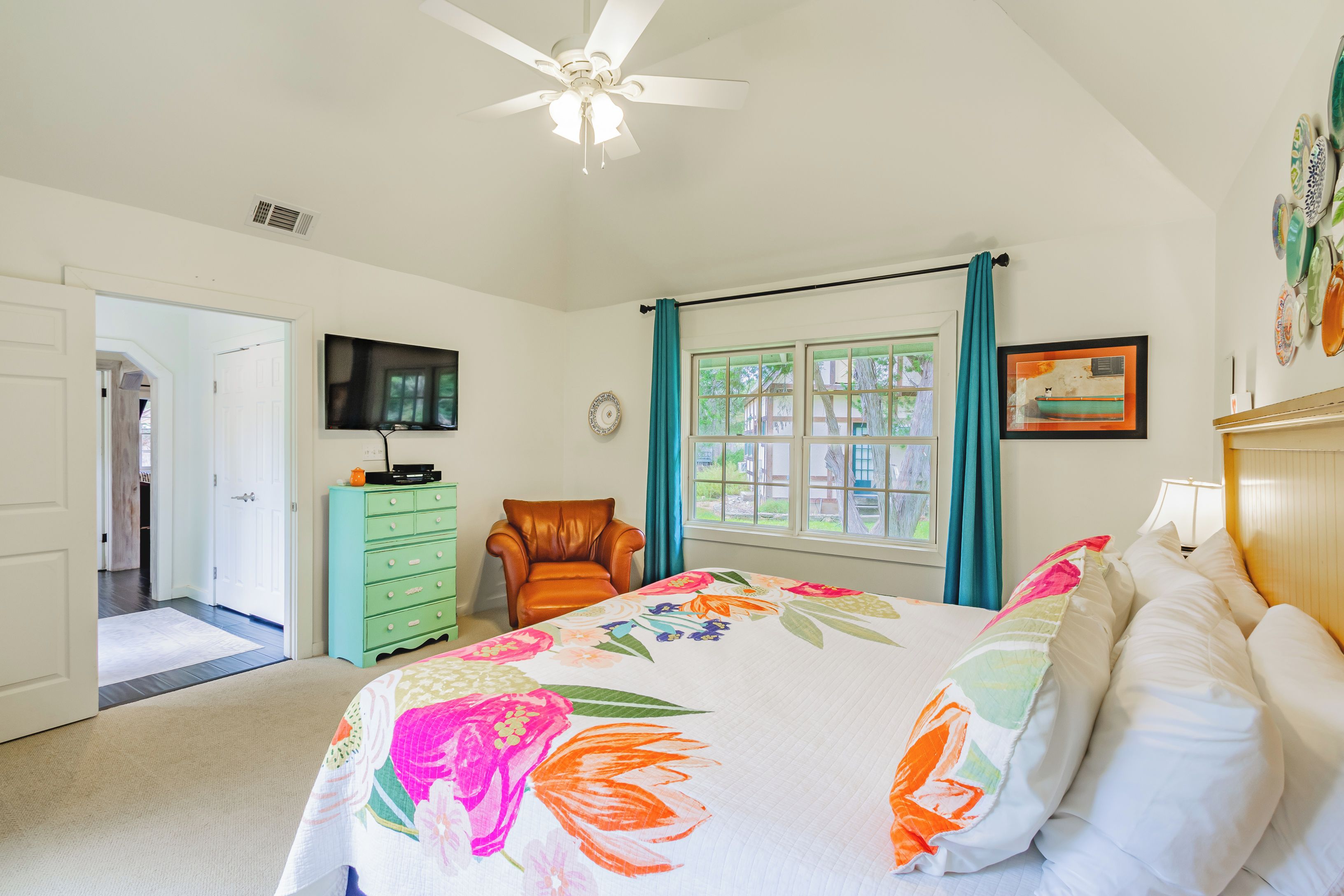 A bedroom with a bed, a chair, a dresser, a television, and a window with curtains.