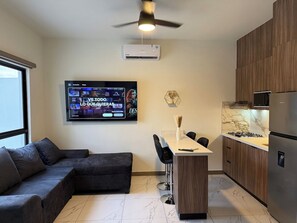 Eine moderne Küche mit Einbauherd, Kühlschrank und Mikrowelle. Es gibt einen Essbereich mit Tisch und Stühlen sowie einen großen Flachbildfernseher an der Wand.