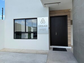 A modern building entrance with a sign reading 'URBAN NEST,' a black door, and a window with a view of the sky. - New Listing (Juárez)