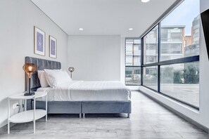 A modern bedroom with a large bed, a bedside table, and a floor lamp. There are two framed pictures on the wall. - New Listing (Bogotá, D.C.)