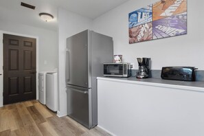 Ett kompakt kök med ett kylskåp i rostfritt stål, en mikrovågsugn, en brödrost och en kaffebryggare på bänkskivan.