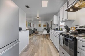 Une cuisine moderne avec des meubles blancs, une cuisinière et un coin repas comprenant une table et des chaises.