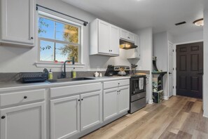 A modern kitchen with white cabinetry, a built-in oven, and a window with a view of trees. - New Keesler/ Beach Walking TMNT Arcade Game (Biloxi)