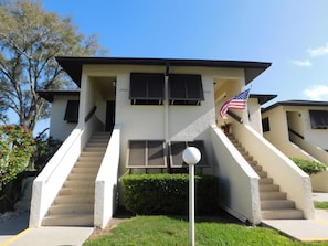 A two-story building with a staircase leading to the entrance, an American flag, and a number '4503' on the wall. - Welcoming 1-bedroom condo in sunny Sarasota with lake views! (Sarasota)