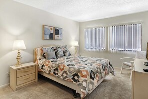 A bedroom with a bed, bedside lamps, a desk, and a window with blinds. - Welcoming 1-bedroom condo in sunny Sarasota with lake views! (Sarasota)