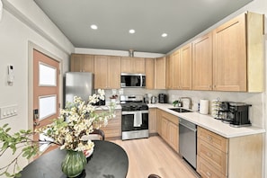 A modern kitchen with wooden cabinets, stainless steel appliances, and a dining area with a vase of flowers.