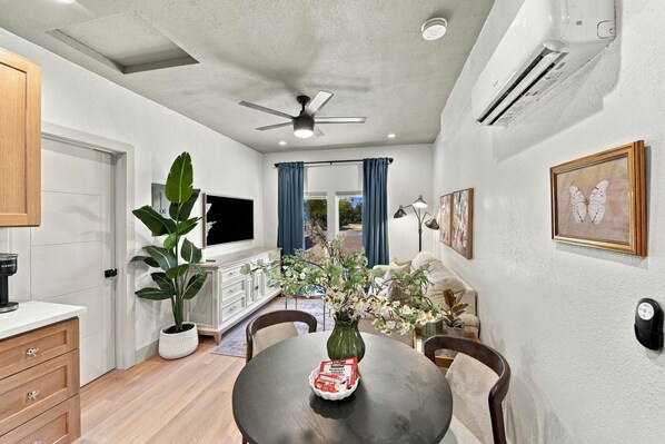 A compact living space with a dining table, chairs, a television, and a ceiling fan.