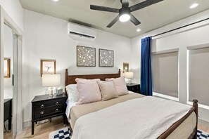 A bedroom with a bed, nightstands, a ceiling fan, an air conditioner, and a window with curtains.