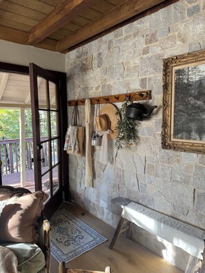A room with a stone wall, a wooden bench, a table, and a window with a view of trees. - Le Miel Cottage Romantic 1923 Forest Escape (Lake Arrowhead)