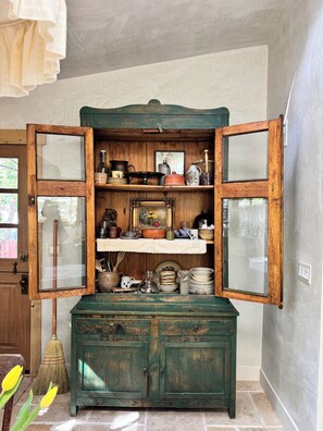Un vieux buffet en bois, doté de portes en verre, renfermant divers ustensiles de cuisine et une photographie encadrée.