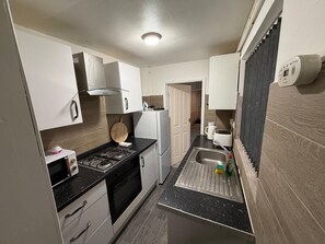 Une cuisine compacte avec des meubles blancs, une cuisinière à gaz, un four encastré, un évier avec une planche à découper et un grille-pain.