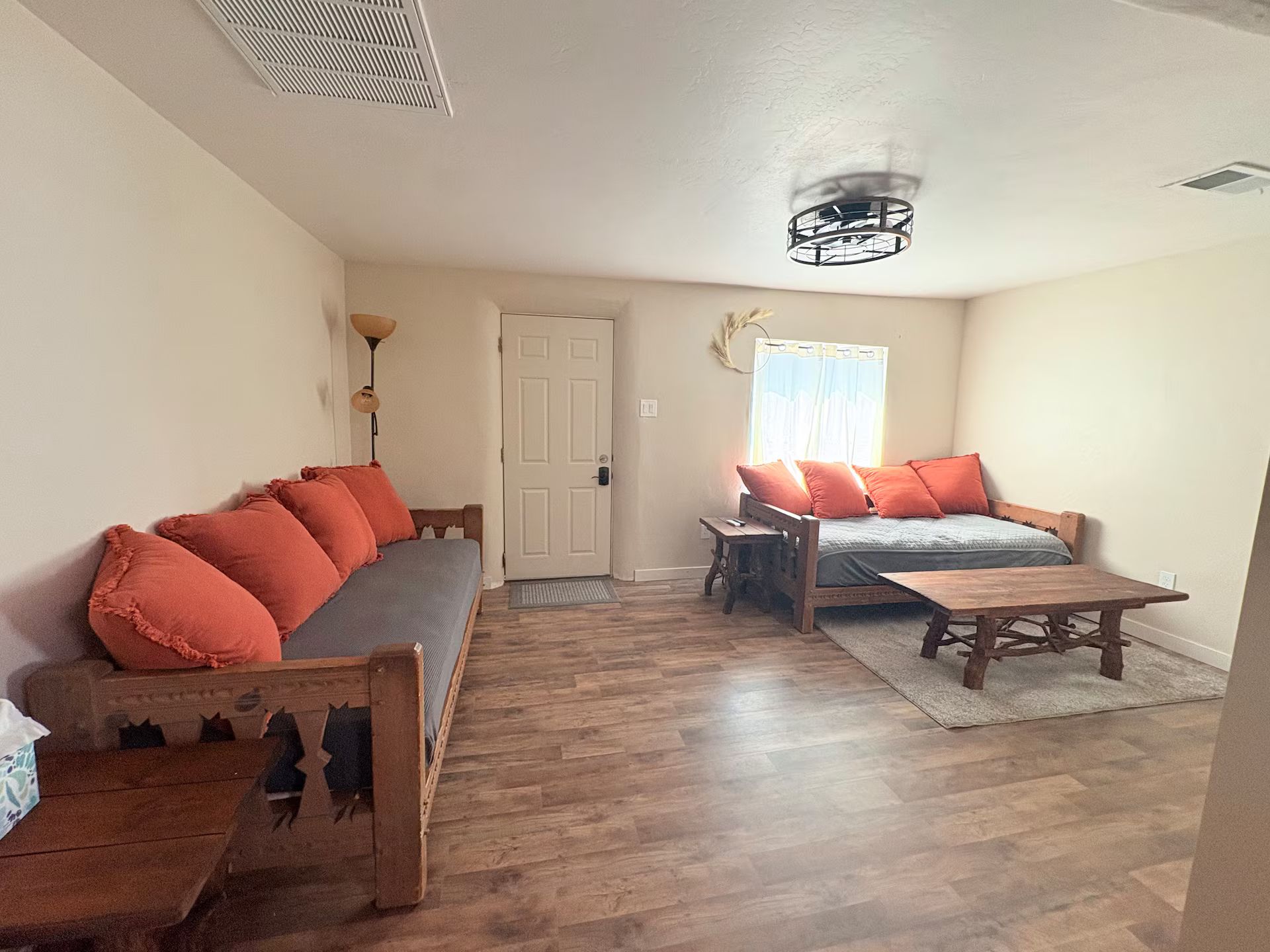 Een ruime woonkamer met een bank, een houten bijzettafeltje en een bed met bijpassende kussens.