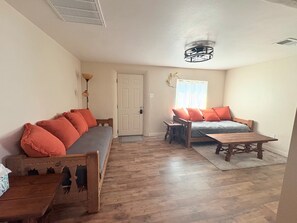 Ein geräumiges Wohnzimmer mit einer Couch, einem Holztisch und einem Bett mit passenden Kissen.