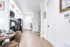 A modern kitchen with stainless steel appliances, a dining area with a wooden table and chairs, and a hallway leading to a door. - By Yale | Sleeps 6 | Sauna + Gym | Free Parking (New Haven)