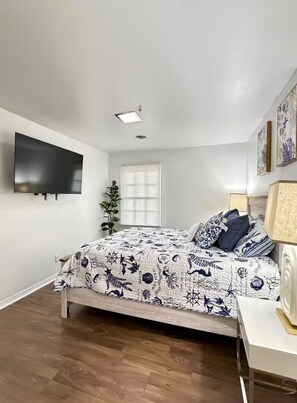 A bedroom with a bed, a flat-screen TV mounted on the wall, a window with blinds, and a plant. - Peaceful Family Home . Minutes from Beaches & Attractions (Fort Walton Beach)