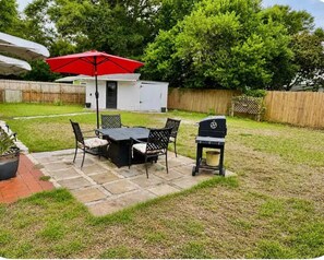 An outdoor patio with a table and chairs, a grill, and a red umbrella. - Peaceful Family Home . Minutes from Beaches & Attractions (Fort Walton Beach)