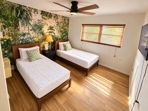 A bedroom with two beds, a ceiling fan, a window with blinds, and a wall-mounted TV. - Bristo At Lantana (Lantana)