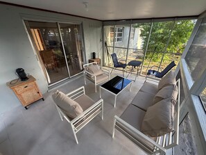 Ein sonnendurchfluteter Raum mit einer Schiebetür zu einer Terrassenanlage, ausgestattet mit einer Couch, Stühlen und einem kleinen Tisch.