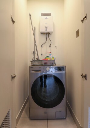 A compact laundry room with a front-loading washing machine, a hose, and a wall-mounted heater. - w* | Chic 1BR w/ Balcony in Miraflores (Miraflores)