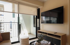 A modern living room with a large TV, a sofa, and a view of the city through floor-to-ceiling windows. - w* | Chic 1BR w/ Balcony in Miraflores (Miraflores)