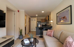 A modern living room with a sofa, coffee table, and a television. A kitchen is visible in the background with a microwave and a sink. - w* | Chic 1BR w/ Balcony in Miraflores (Miraflores)
