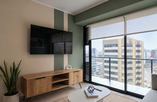 Una sala moderna con un ventanal grande, un televisor de pantalla plana, un mueble de madera y una planta en maceta.