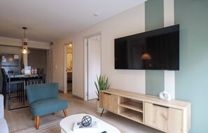 Una sala de estar moderna con un televisor de pantalla plana, un sillón color verde azulado, una mesa de centro y un mueble de madera para equipo de entretenimiento.