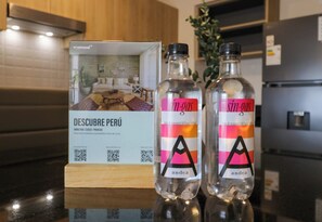 Due bottiglie di 'sin-gas' con etichette e un codice QR, poste su un bancone della cucina con una scatola di legno e un altro codice QR sullo sfondo.