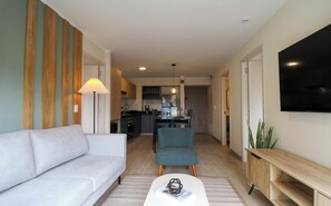A modern living room with a sofa, a dining table with chairs, a kitchen in the background, and a flat-screen TV mounted on the wall. - w* | Fantastic 2BR with Balcony in Miraflores (Miraflores)