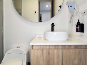 A bathroom with a white sink, a mirror, a hairdryer, and a soap dispenser. - w* | Stylish Loft in the Heart of Chicó Norte (Bogotá)