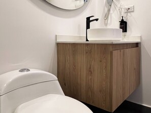 A modern bathroom with a white toilet, a wooden vanity, and a white sink. - w* | Stylish Loft in the Heart of Chicó Norte (Bogotá)