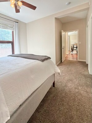 Een slaapkamer met een bed, een plafondventilator, een raam met gordijnen en een vloerbedekking.