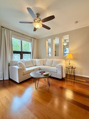 A living room with a sectional sofa, a round coffee table, a ceiling fan, and a lamp. - 2-BD Private Entry 2 Parking Space Corporate apartment in fabulous Downtown SD (San Diego)