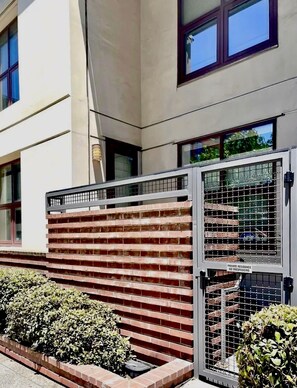 A gated entrance with a metal fence and a brick wall, leading to a building with multiple windows. - 2-BD Private Entry 2 Parking Space Corporate apartment in fabulous Downtown SD (San Diego)