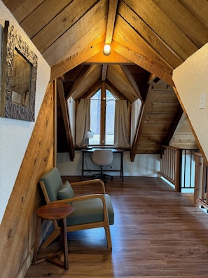A cozy attic room with wooden beams, a desk, a chair, and a large window. - Cozy Cabin with a Fireplace and a Hot Tub (flagstaff)
