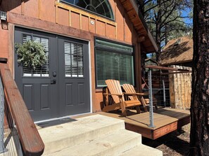 A two-story house with a grey front door, a wooden deck with two chairs, and a staircase leading to the upper level. - Cozy Cabin with a Fireplace and a Hot Tub (flagstaff)