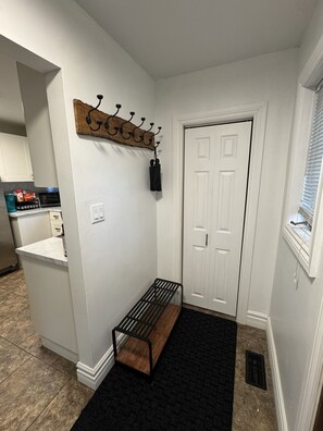 A hallway with a coat rack, a bench, a door, and a kitchen area in the background. - North Nook (Barrie)