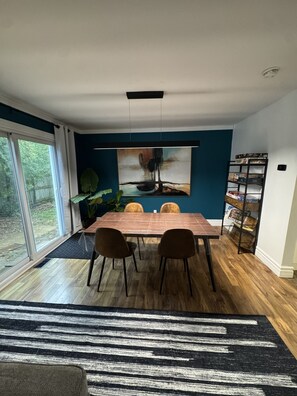 A dining area with a table, chairs, a large abstract painting, a plant, and a bookshelf. - North Nook (Barrie)