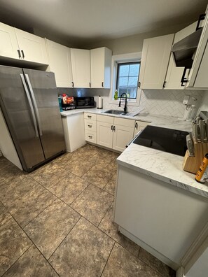 A kitchen with white cabinets, a stainless steel refrigerator, a microwave, and a sink. - North Nook (Barrie)