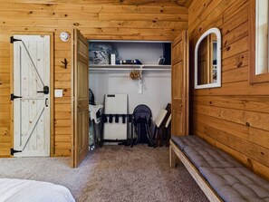 Una habitación de madera con cama, un banco, un radiador, un escritorio y un espejo.