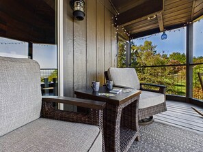 Un espacio de estar techado al aire libre con mobiliario de mimbre y una mesa, con vistas a un jardín.