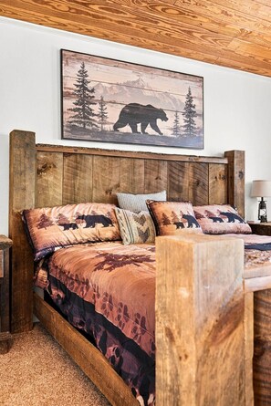 Un dormitorio con cabecera de madera, cama con colcha temática de oso y un cuadro con la silueta de un oso sobre la cama.