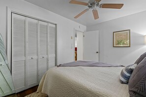 Et soveværelse med seng, ventilator, garderobeskab og dør til et andet rum.