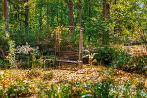 A garden with a metal bench surrounded by foliage and fallen leaves. - The Koi Cottage: Hot Tub - Treehouse - BIG Pond. 5 years as a top rated retreat! (Maggie Valley)