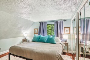 Ein Schlafzimmer mit einem großen Bett, zwei Nachttischen, einem fensterbelaubten Fenster und einem Spiegel mit Blick auf Grün.