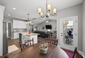 A modern kitchen with white cabinets, a central island, and a dining area with a wooden table and chairs. - Family Home - Near SIUE - 3BR/2BA (Glen Carbon)