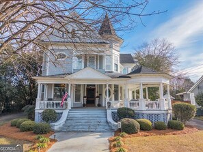 A two-story house with a porch, a small gazebo, and a flag. - The Grey Lady: 1910 Victorian, Sleeps 12, Walk to Downtown Americus (Americus)