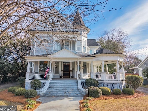 A two-story house with a porch, a small gazebo, and a flag.
