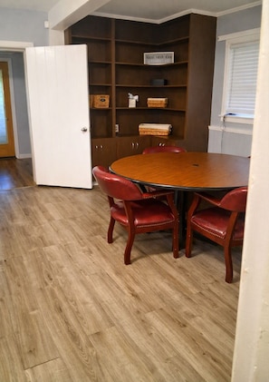 A dining area with a round table and four red chairs, a wooden floor, and a bookshelf with various items. - Neal Street Retreat - Welcoming Home, Perfect for Families and Getaways (Tuskegee)